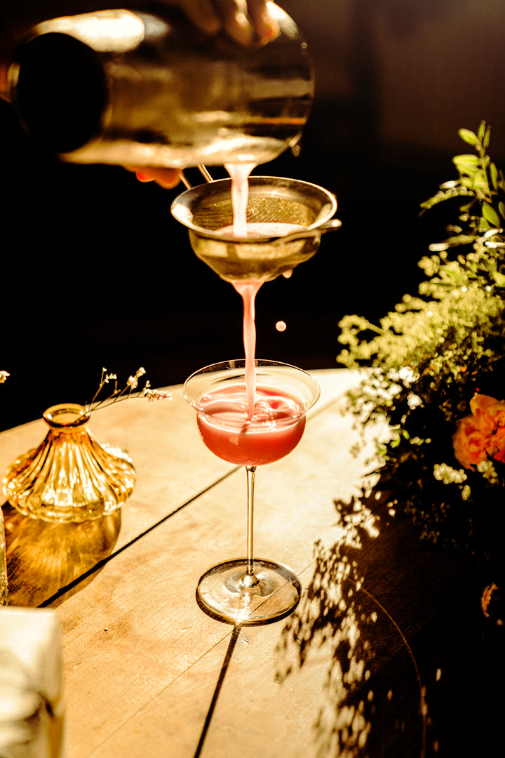A cocktail being strained into a coupe glass